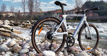 Fiido Air ultralichte elektrische fiets van koolstofvezel, opgesteld op een rotsachtige rivieroever naast stromend water.