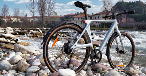Fiido Air ultralichte elektrische fiets van koolstofvezel, opgesteld op een rotsachtige rivieroever naast stromend water.