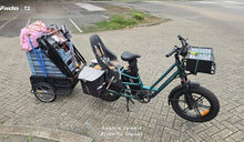 Een Fiido T2 elektrische bakfiets is volledig beladen met een kinderzitje, zijtassen, een voorste laadbak en een zwaar beladen aanhanger.